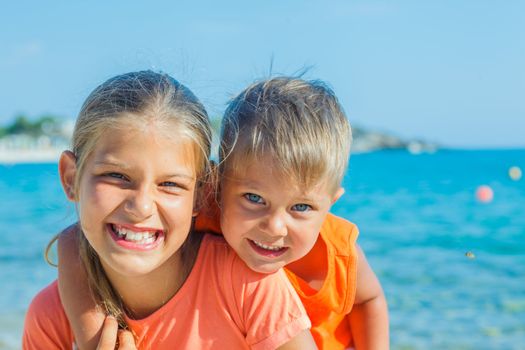 Smiling happy brother and sister posing on a beach. In the background the sea