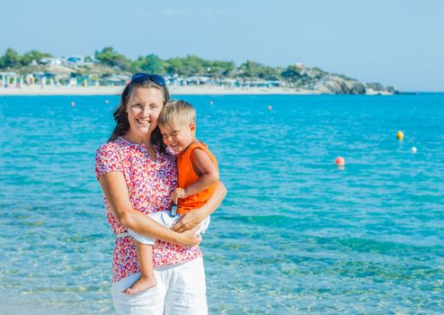 Portrait of happy mother with son laughing and looking at camera on the beach