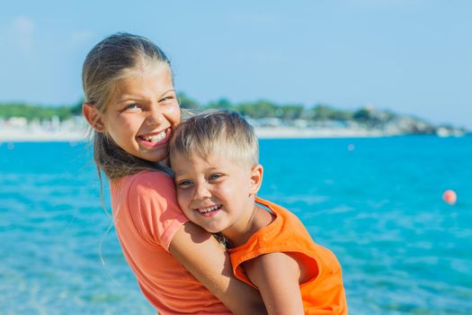 Smiling happy brother and sister posing on a beach. In the background the sea