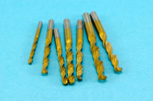 various size golden color drill bits on blue background.
