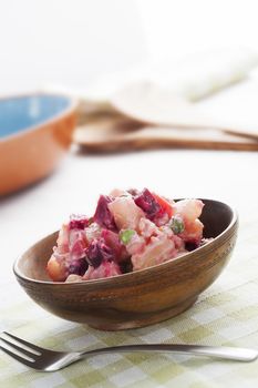 Haitian potato salad, salad pomdete, made with potatoes, carrots, beetroot, peas, bell peppers and eggs.  In small wooden bowl, vertical orientation