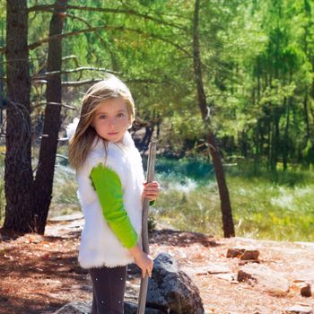 Explorer blond kid girl sith stick and winter white fur in pine forest ourdoor