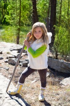Explorer blond kid girl sith stick and winter white fur in pine forest ourdoor