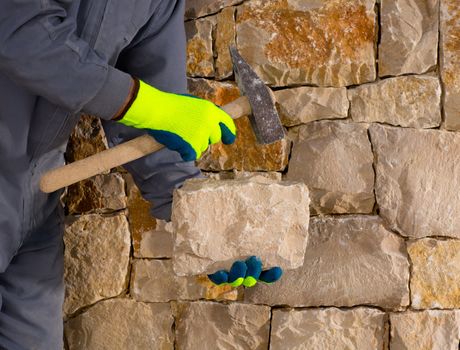 stonecutter mason with hammer and stone building a masonry stone wall