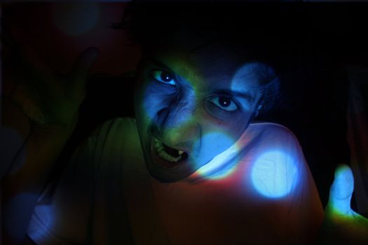 A portrait of a young Indian guy with mad and scary expressions in party lights.