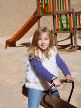 Blond child girl playing in playground smiling on swing with winter fur