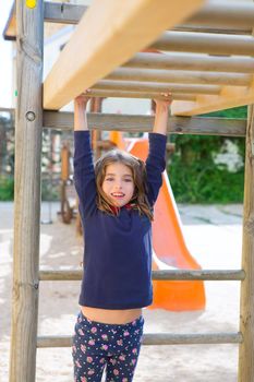 kid girl playing in playground hanging from wood bars smiling happy