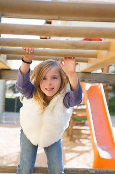 kid girl playing in playground hanging from wood bars smiling happy