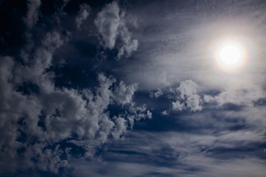 Dark blue sky with scattered clouds and sun
