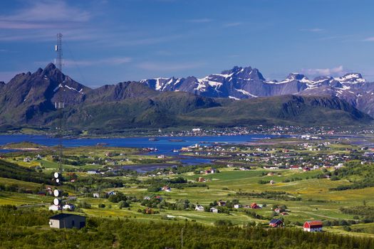 Scenic panorama with green meadows, town of Leknes and snowy peaks of picturesque Lofoten islands in Norway