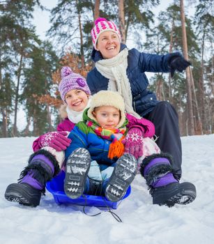 Mother with her two kids is sledging in winter-landscape. Focus on the boy.