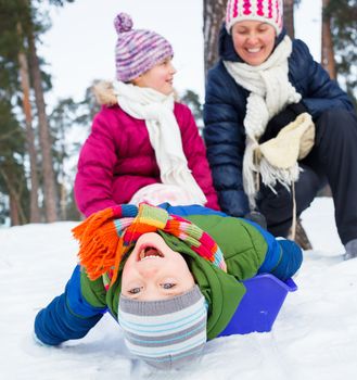 Mother with her two kids is sledging in winter-landscape. Focus on the boy.