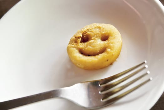 Generic shot of Reconstituted deep fried potato shaped like a smiley face plated with a steel fork