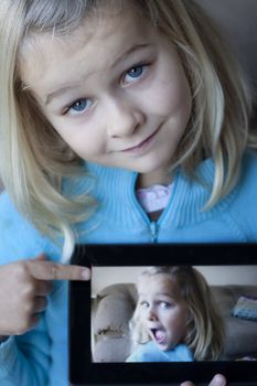 A cute girl holding a tablet which shows a blurred photo of herself