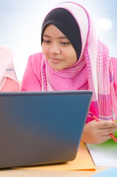 Muslim girls. Southeast Asian Muslim college girls discussing, looking on laptop screen, indoor.