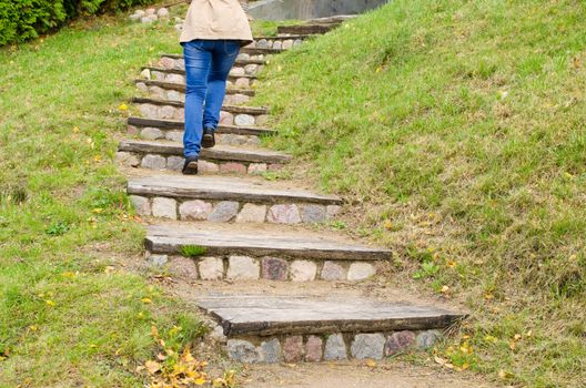 woman legs in blue jeans climb on retro rural stone and wood stairs.