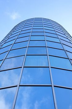 round facade of office building with blue sky and clouds reflected