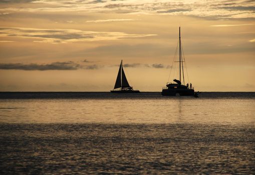 Sailing boat and catamaran on the horizon as the sun goes down