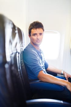 Handsome young man on board of an airplane during flight,  looking at the camera with a relaxed, confident expression