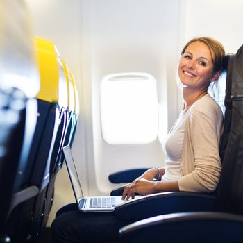 Young woman working on her laptop computer on board of an airplane during the flight