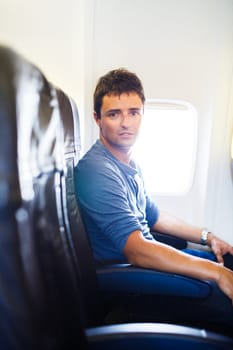Handsome young man on board of an airplane during flight,  looking at the camera with a relaxed, confident expression
