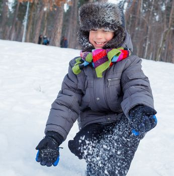 Cute boy plaing with snow in winter forest.