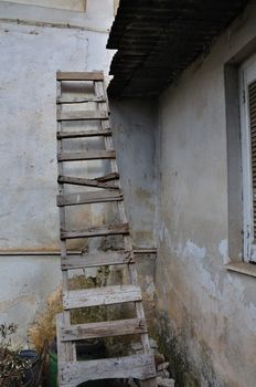 Wooden broken ladder leaned against peeling wall of abandoned house.