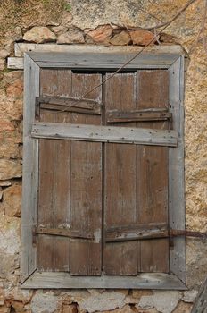 Boarded up wooden window shutter and weathered wall of derelict house.