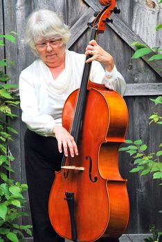 Mature female cellist with her instrument outside.