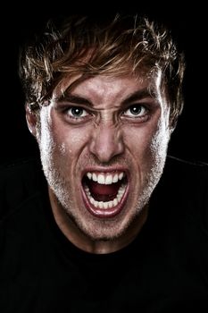 Man screaming angry aggressive at camera on black background. Young Caucasian mad male model.