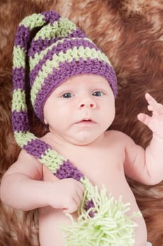 Shot of newborn baby in long striped hat lying on fur