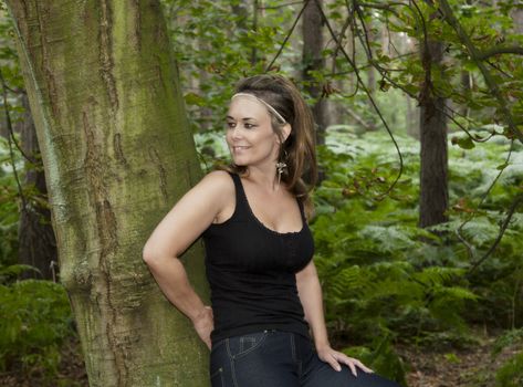 attractive woman in woodland setting leaning against a tree
