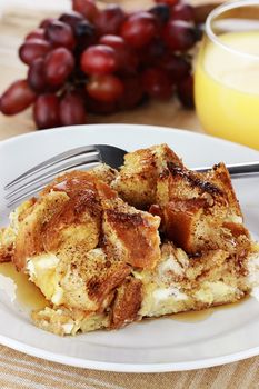 French toast casserole with maple syrup. Made with cream cheese cheese in the center. Fresh grapes and orange juice in background. Extreme shallow depth of field with selective focus on French toast.

