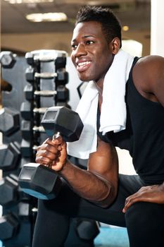 Young gym instructor toning his biceps, triceps and forearm while exercising with heavy dumbbell