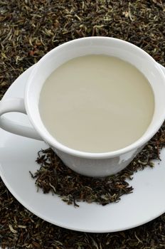 Black tea with milk standing on dried black tea leaves.