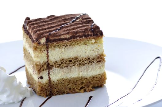 A dessert of tiramisu on a white plate with chocolate and cream. 