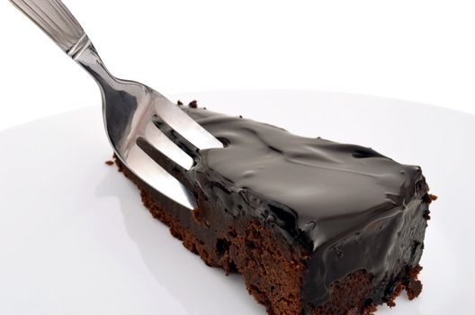 A piece of a tasty dark chocolate cake on a white plate with a fork.