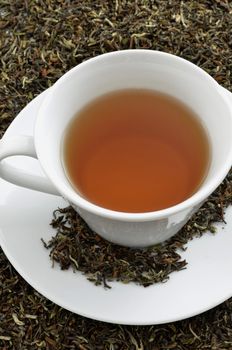 A cup of black tea standing on dried black tea leaves.