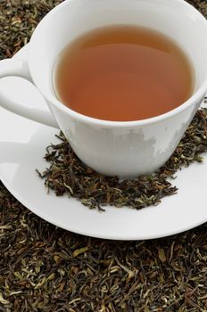 Closeup of a black tea standing on dried black tea leaves.