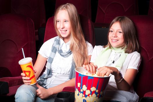 teen girls in the movie theater, holding popcorn and a drink and look at the screen