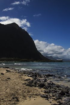 rock and sand beach by the base of a hawaiin mountain