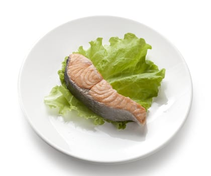 Piece of steamed salmon with fresh lettuce on the white plate