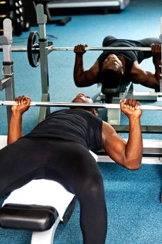 An african male bodybuilder trying to lift the barbell. Reflection can be seen in the mirror
