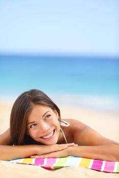 Beach woman thinking looking up at copyspace. Multiracial Asian Chinese / Caucasian female girl relaxing on beach towel smiling happy.