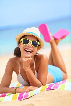 Beach woman laughing having fun in summer vacation holidays. Multiracial fashion hipster wearing sunglasses lying in the sand on colorful beach towel.