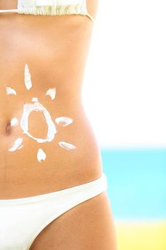Sunscreen / sunblock woman. Solar cream protection drawing on suntan stomach of tan beautiful woman in bikini on sunny beach.