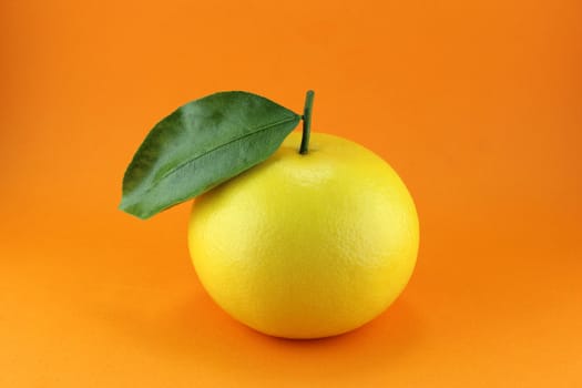 Ripe appetizing grapefruit with leaf on orange background.