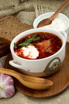 Ukrainian National Traditional Soup with Beet, Vegetables and Meat. Arrangement with Dish of Borscht with Brown Bread, Garlic and Sour Cream on Wooden Plate with Wooden Spoon