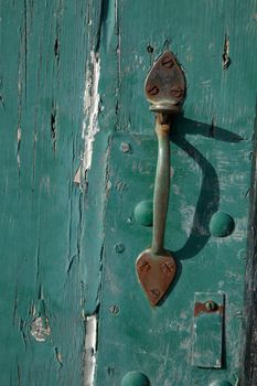 An old brass latch handle with rusty screw heads on a green flaky painted door.