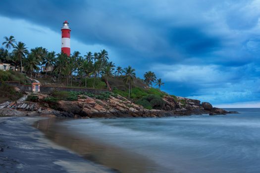 Gathering storm on beach and Kovalam (Vizhinjam) lighthouse on stormy sunset. Kerala, India